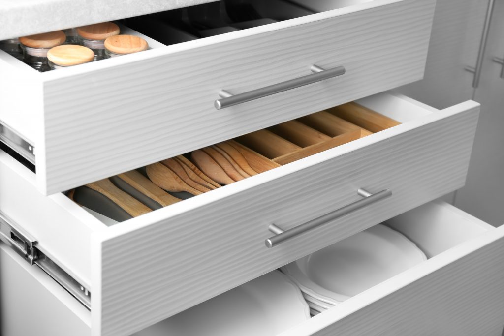 White, open kitchen drawers showing set of ceramic plates and utensils