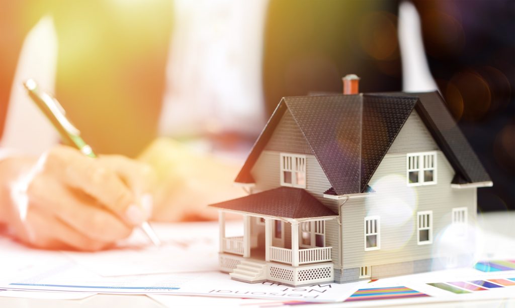 Mini house on desk and businessman holding pen background, bokeh